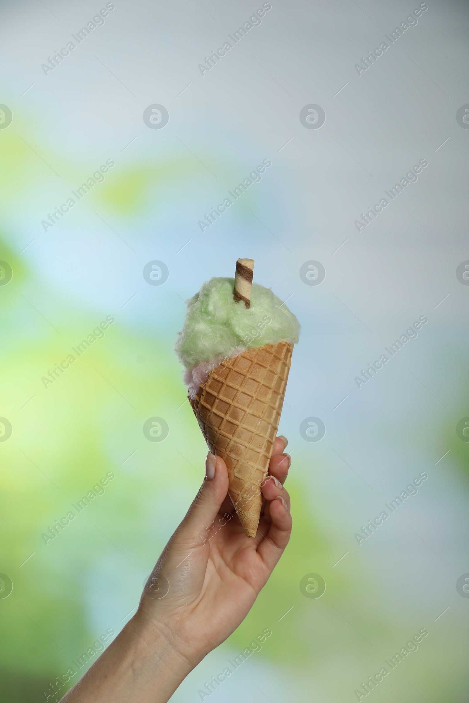 Photo of Woman holding waffle cone with cotton candy on blurred background, closeup