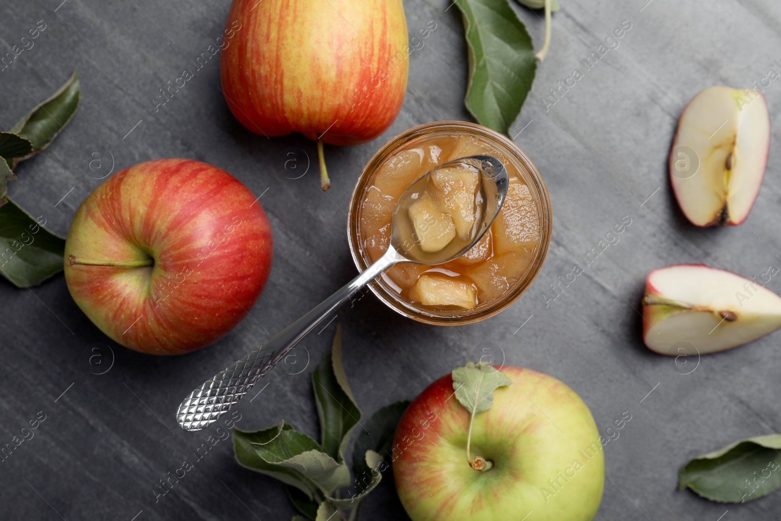 Photo of Tasty apple jam in glass jar and fresh fruits on grey table, flat lay