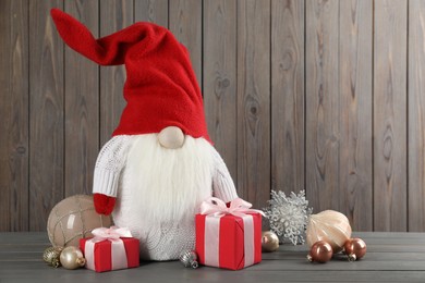 Photo of Cute Christmas gnome, gift boxes and festive decor on wooden table. Space for text