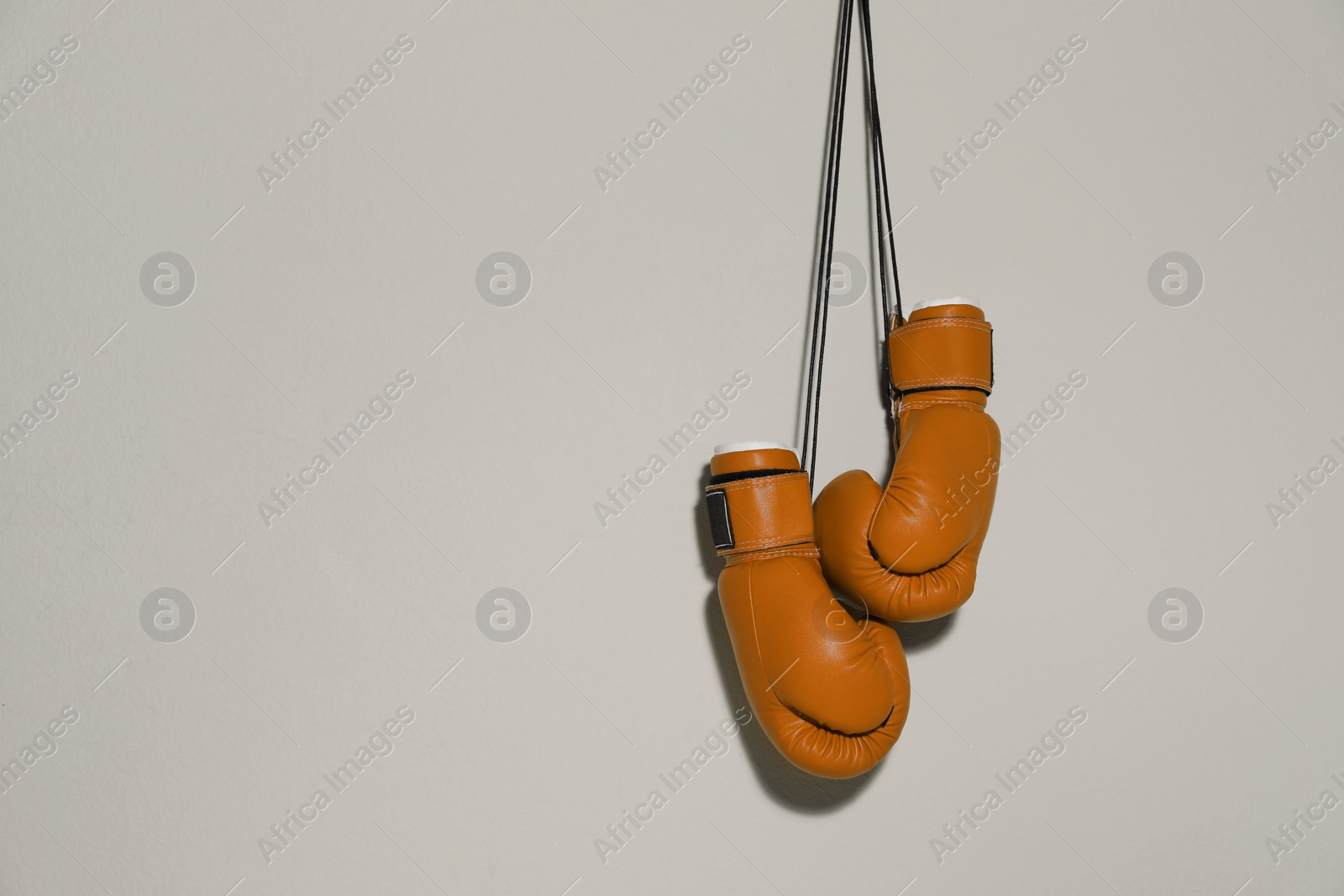 Image of Pair of boxing gloves hanging on light grey wall, space for text