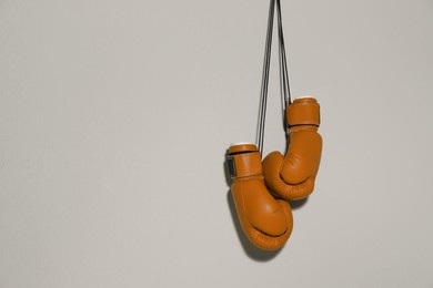 Image of Pair of boxing gloves hanging on light grey wall, space for text