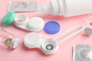 Photo of Cases with color contact lenses, bottles of solution and tweezers on pink background