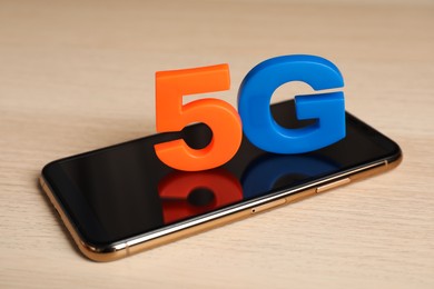 Photo of 5G technology, Internet concept. Smartphone with number and letter on wooden table, closeup