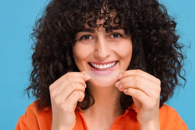 Young woman applying whitening strip on her teeth against light blue background