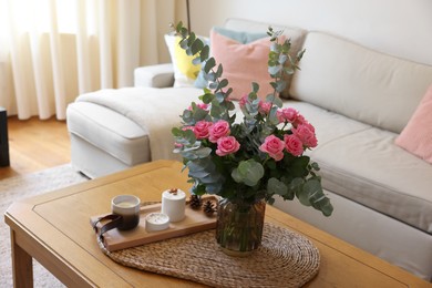 Photo of Beautiful bouquet of roses and eucalyptus branches in vase near candles on table in room