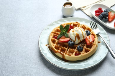 Delicious Belgian waffles with ice cream, berries and caramel sauce served on grey table, closeup. Space for text