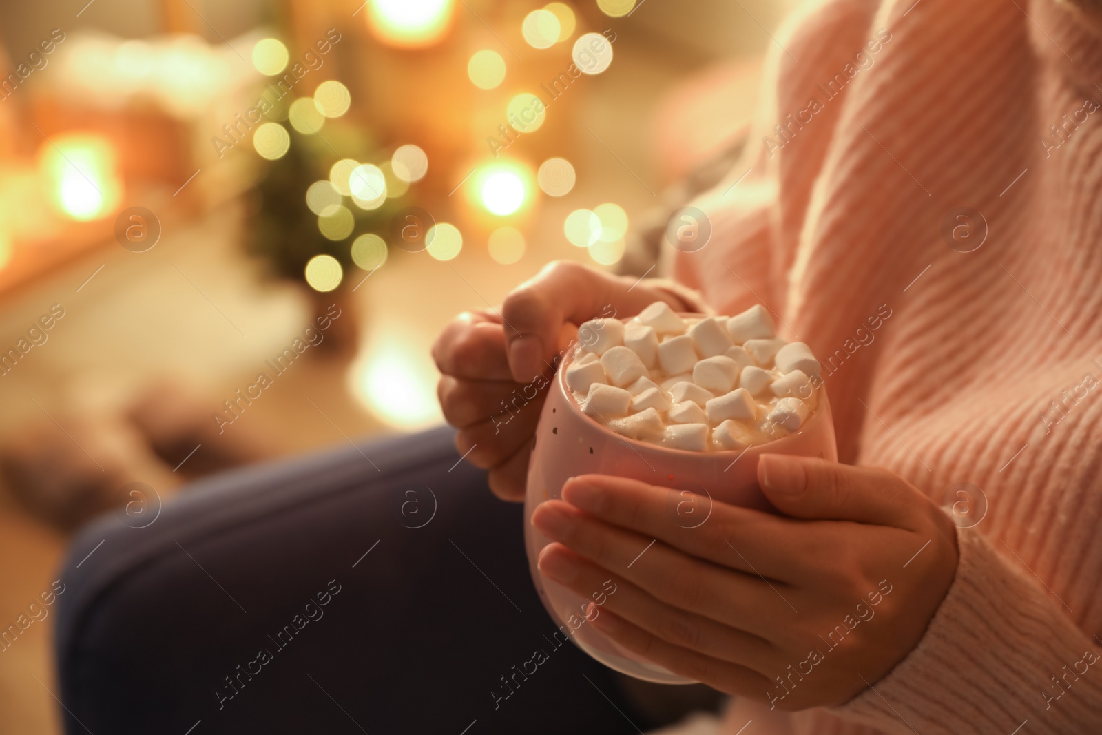 Photo of Woman holding cup of hot drink with marshmallows indoors, closeup. Magic Christmas atmosphere