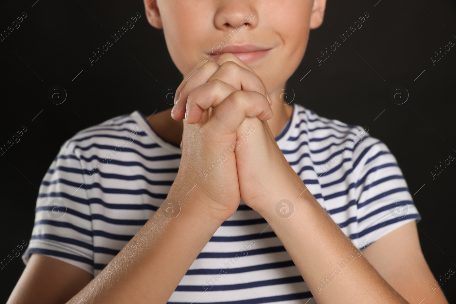 Photo of Boy with clasped hands praying on black background, closeup