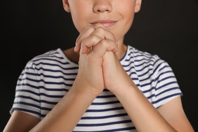 Photo of Boy with clasped hands praying on black background, closeup