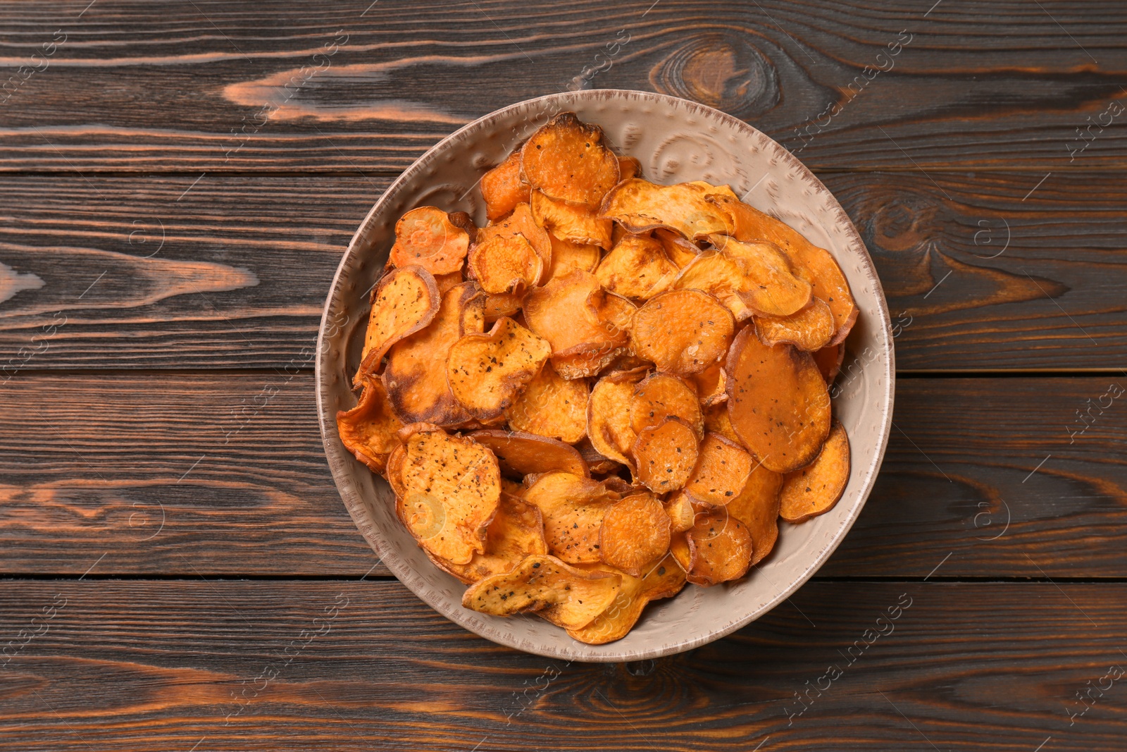 Photo of Plate of sweet potato chips on wooden table, top view