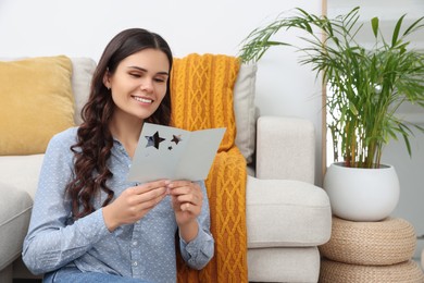 Young woman with greeting card on floor in living room