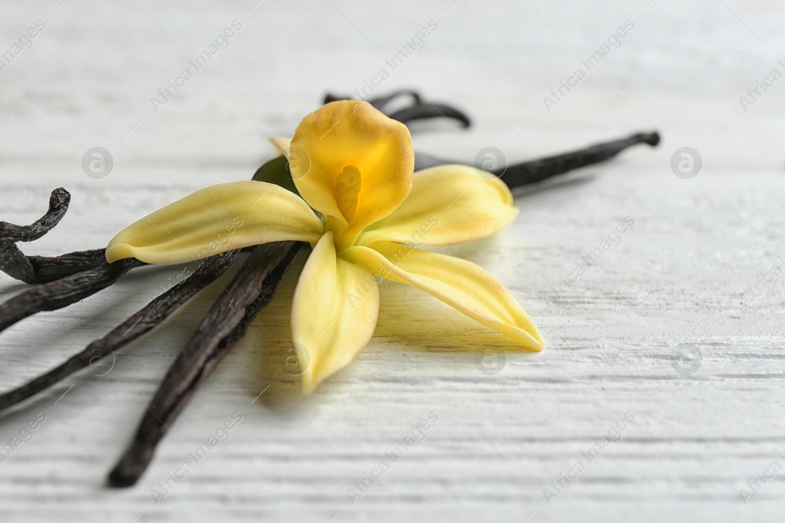 Photo of Vanilla sticks and flower on wooden background, closeup. Space for text