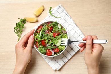 Photo of Woman eating delicious salad with arugula and vegetables at wooden table, top view