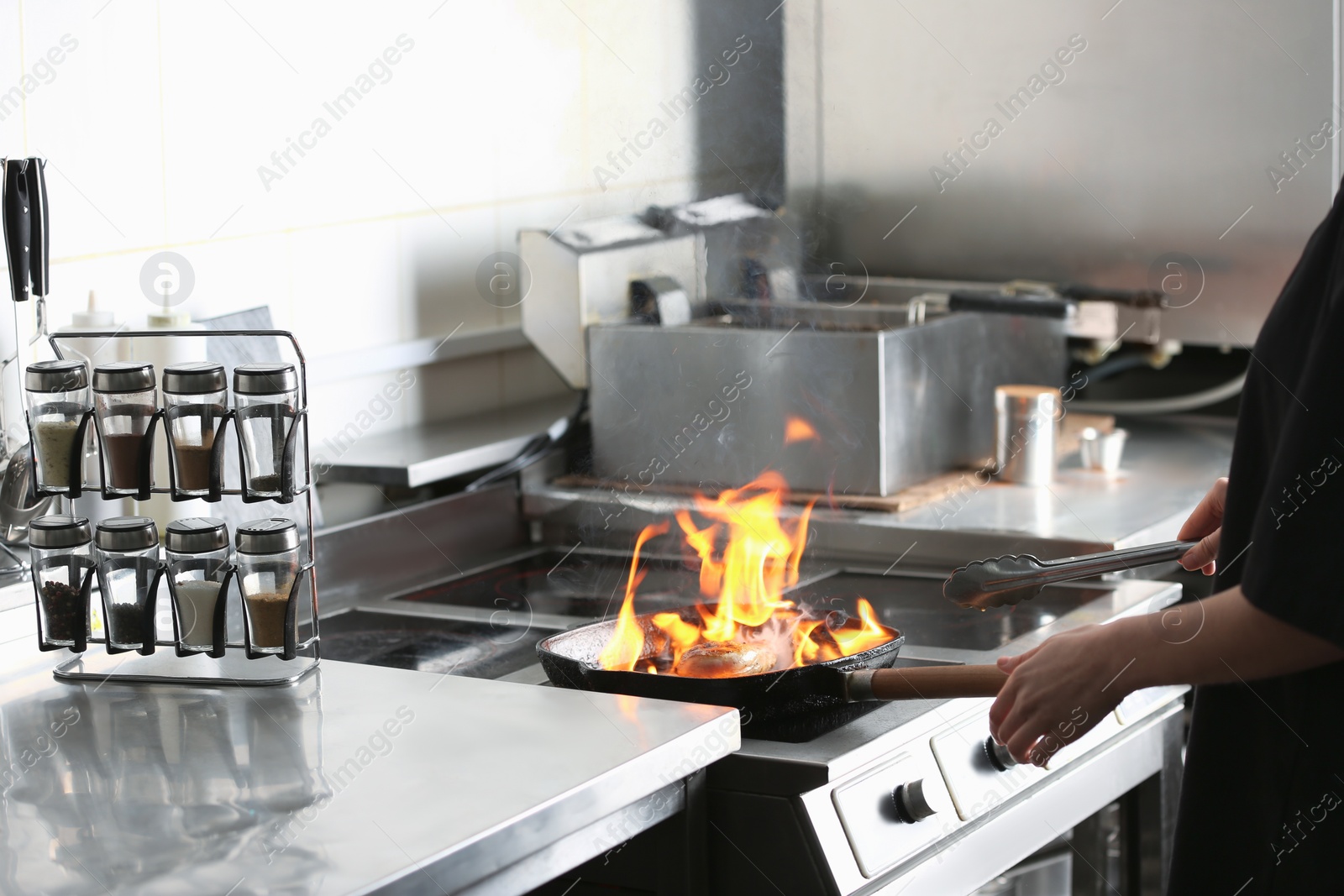 Photo of Female chef cooking meat with burning flame on stove in restaurant kitchen, closeup