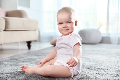 Photo of Cute little baby sitting on soft carpet indoors