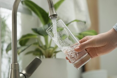 Photo of Woman filling glass with water from tap at home, closeup