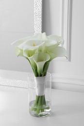 Photo of Beautiful calla lily flowers tied with ribbon in glass vase on white table