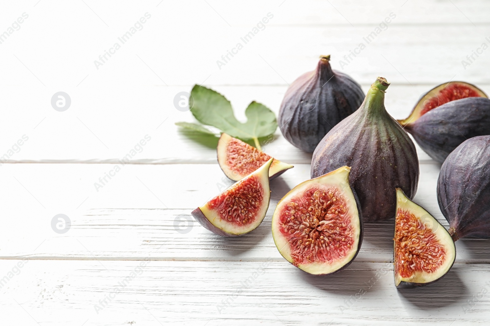 Photo of Whole and cut purple figs on wooden background. Space for text