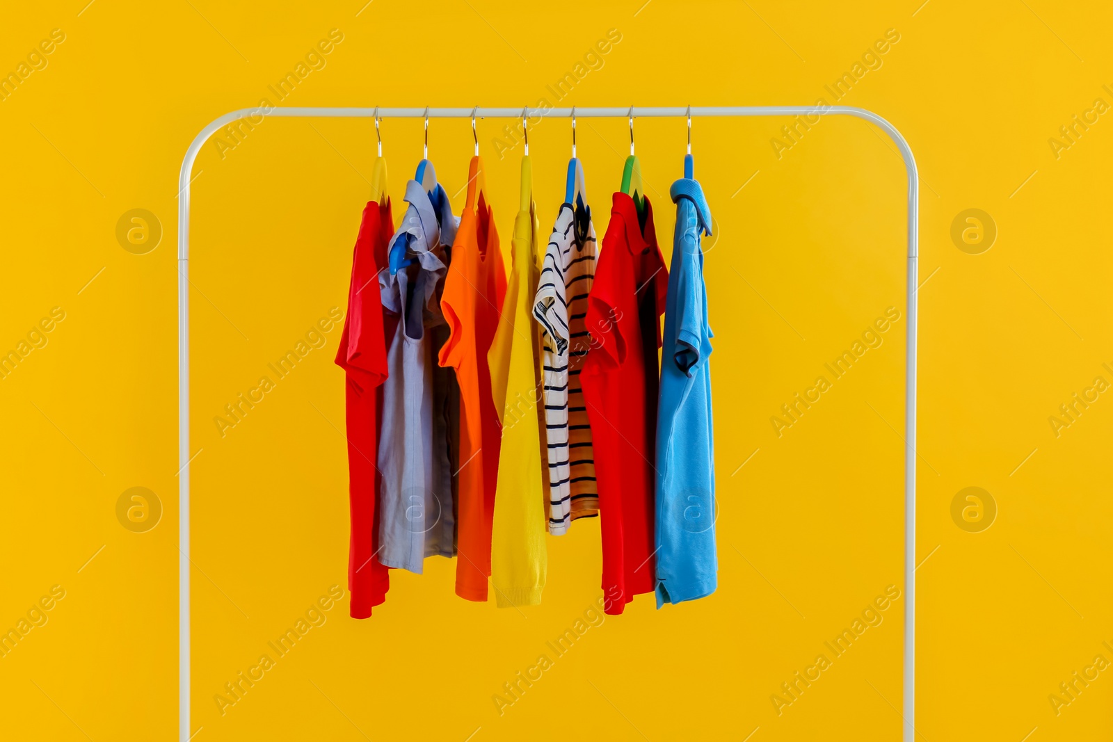 Photo of Rack with stylish children clothes on yellow background