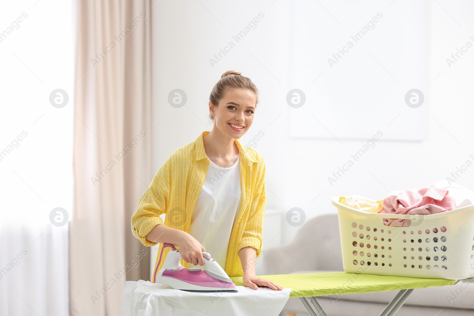 Photo of Young pretty woman ironing clean laundry indoors