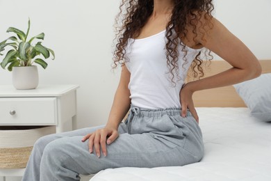 Photo of African American woman suffering from back pain after sleeping on uncomfortable mattress in bedroom, closeup