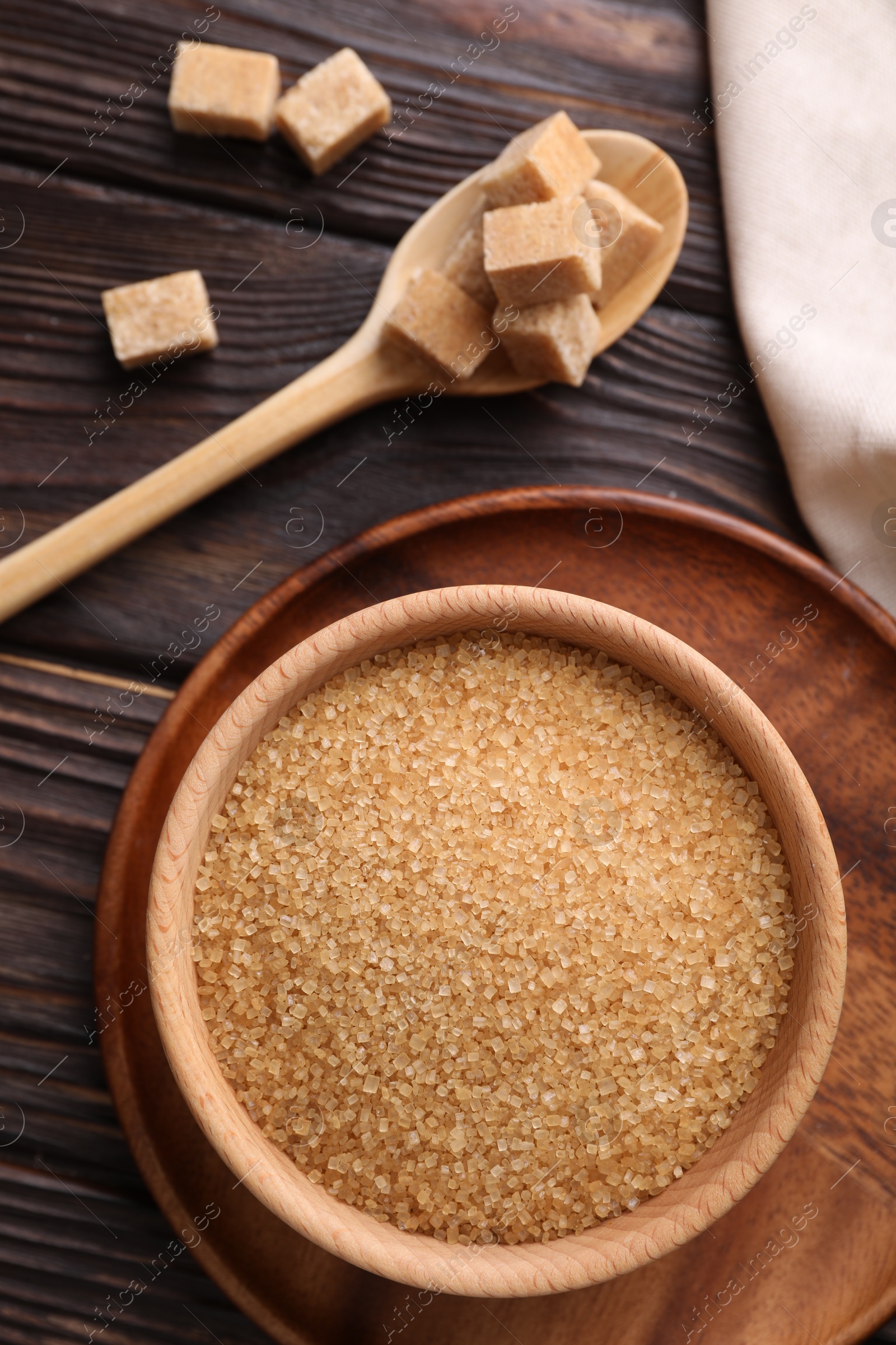 Photo of Bowl and spoon with brown sugar on wooden table, flat lay