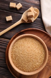 Bowl and spoon with brown sugar on wooden table, flat lay