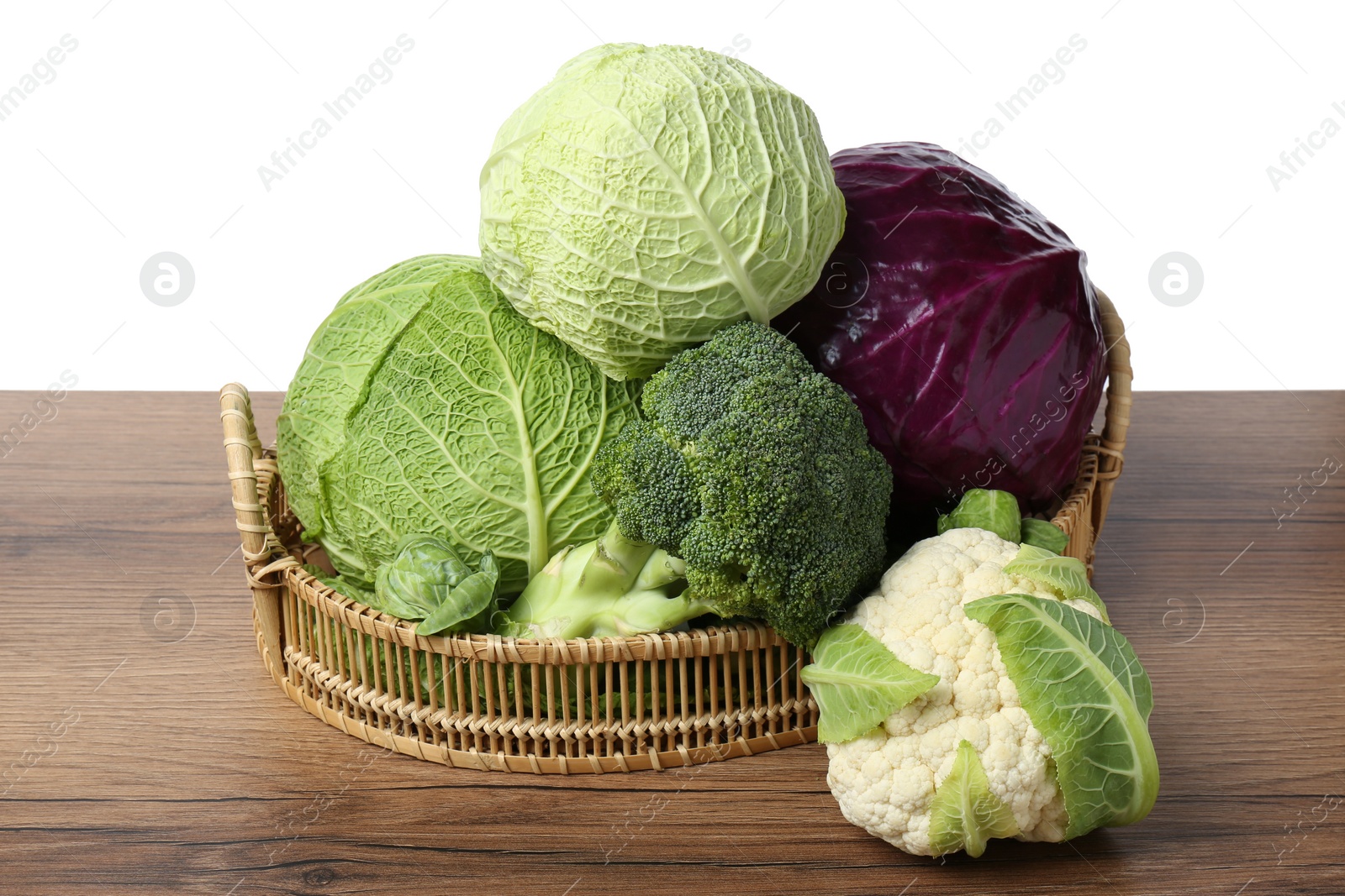 Photo of Wicker tray with different types of fresh cabbage on wooden table against white background