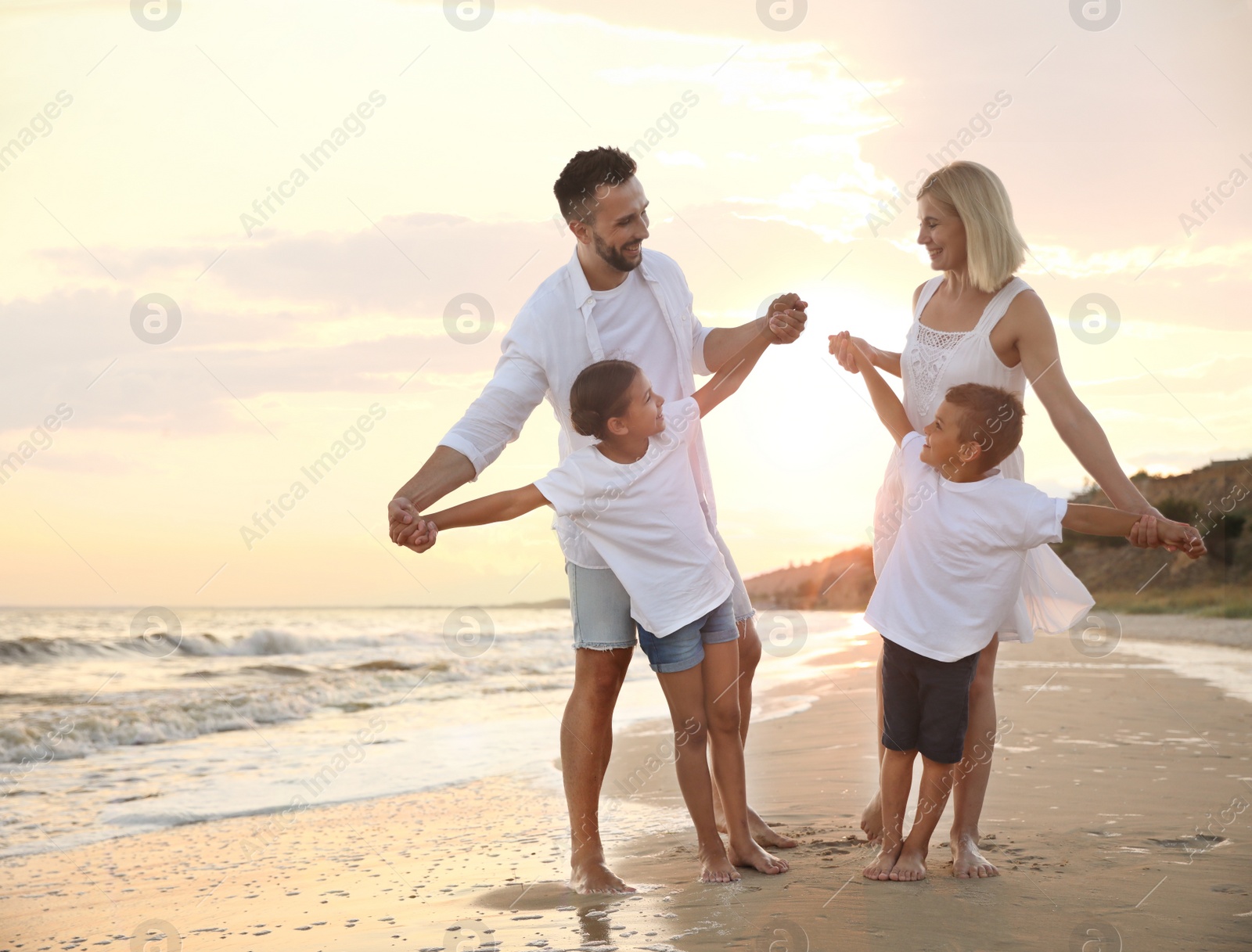 Photo of Happy family having fun on sandy beach near sea at sunset