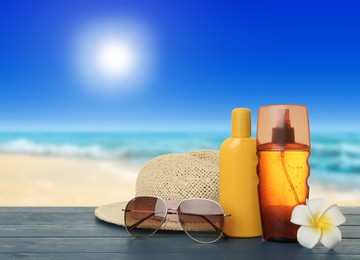 Image of Skin sun protection products and beach accessories on blue wooden table against seascape. Space for design