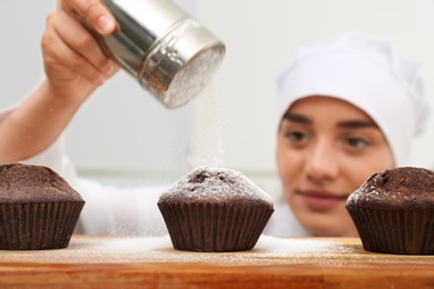 Photo of Female pastry chef sprinkling cupcakes with sugar powder in kitchen