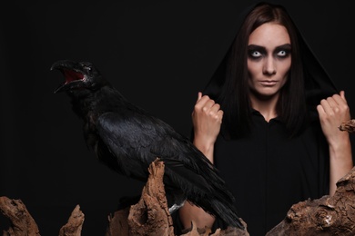 Raven and mysterious witch on black background