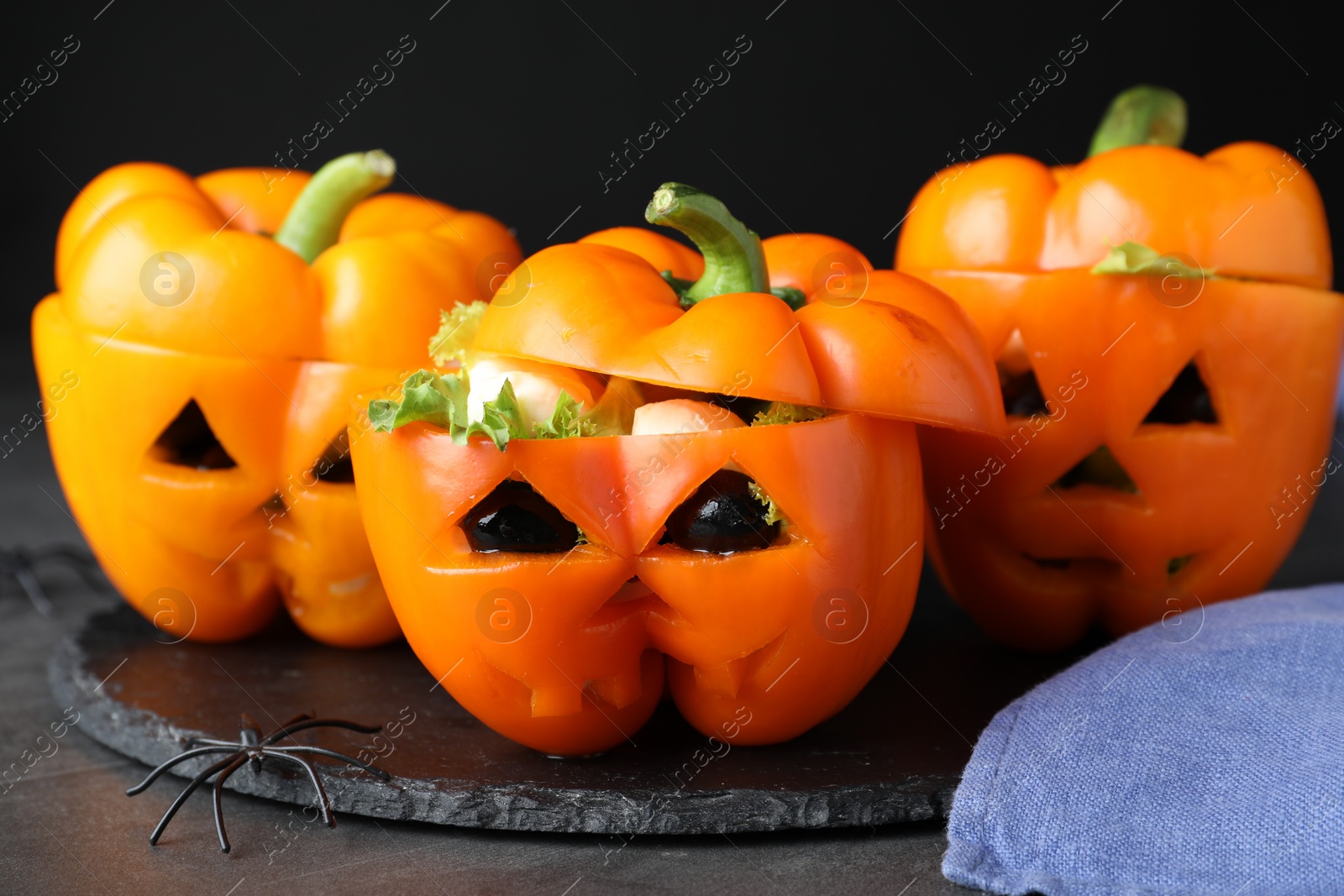 Photo of Bell peppers with black olives, mozzarella and lettuce as Halloween monsters on dark table, closeup