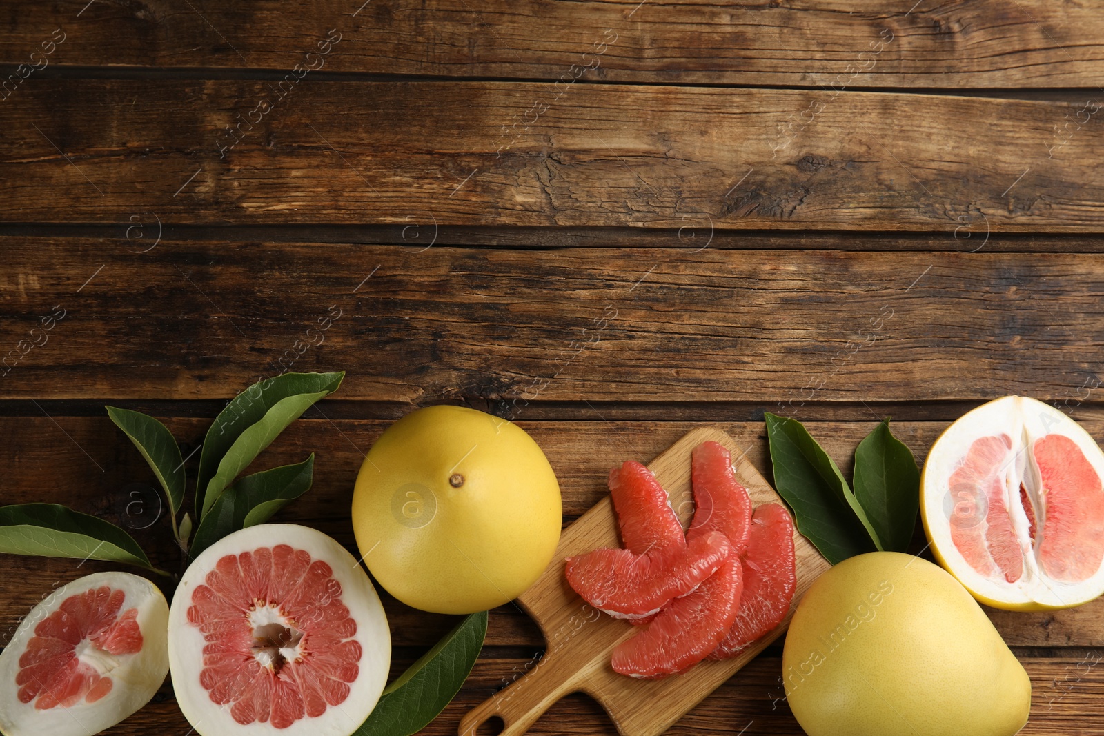 Photo of Fresh cut and whole pomelo fruits with leaves on wooden table, flat lay. Space for text