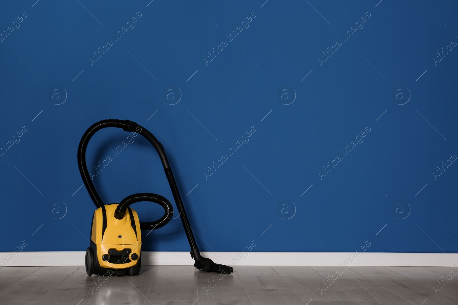 Photo of Modern yellow vacuum cleaner on floor near blue wall, space for text