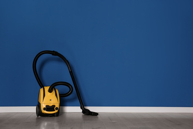 Modern yellow vacuum cleaner on floor near blue wall, space for text