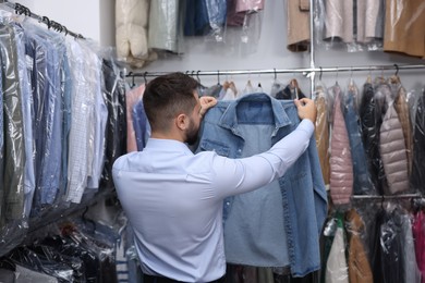 Photo of Dry-cleaning service. Worker holding denim shirt indoors