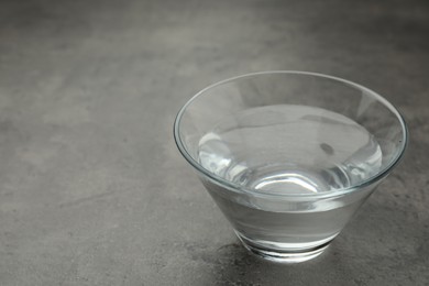 Glass bowl with water on grey table. Space for text