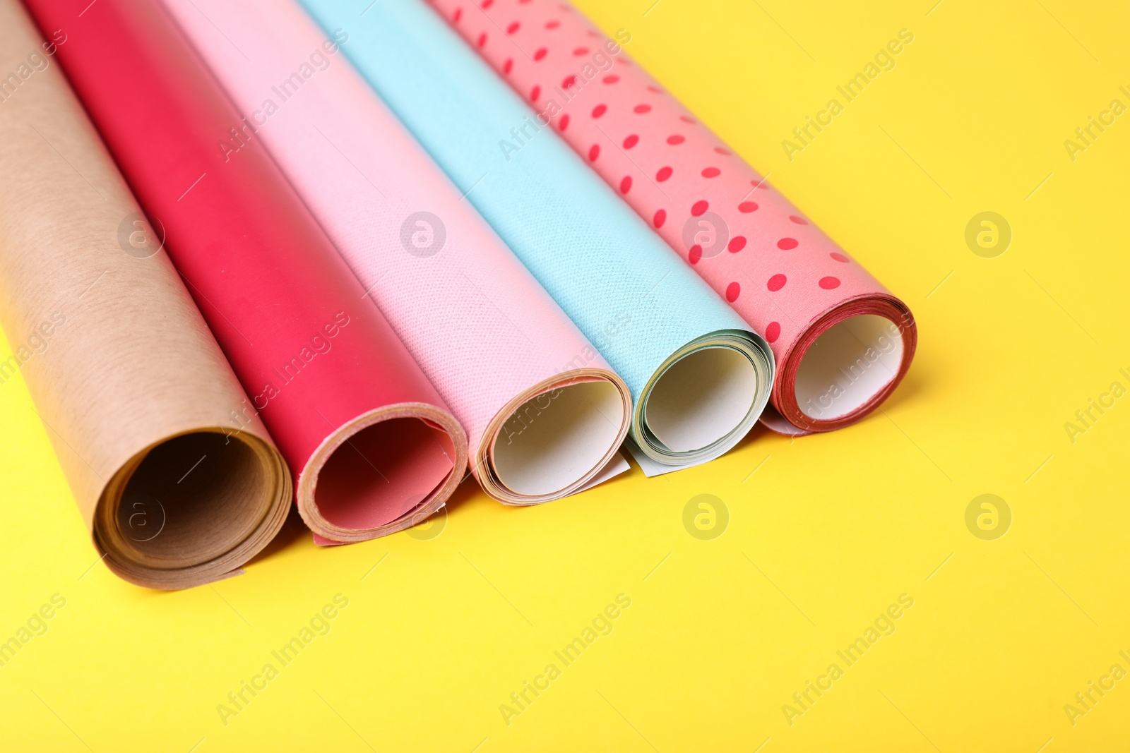 Photo of Rolls of colorful wrapping papers on yellow background, closeup