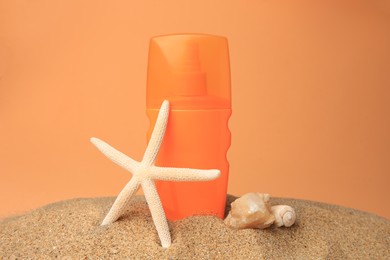 Photo of Sand with bottle of sunscreen, starfish and seashells against orange background. Sun protection