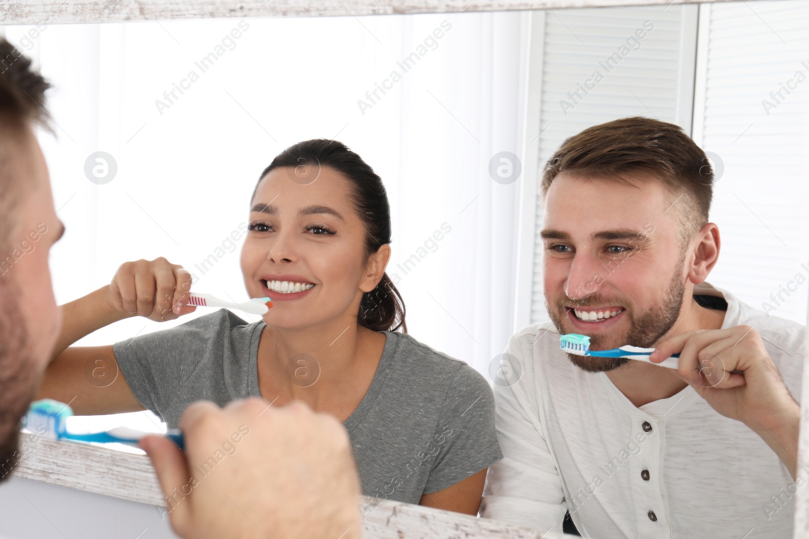 Photo of Young couple cleaning teeth against mirror in bathroom