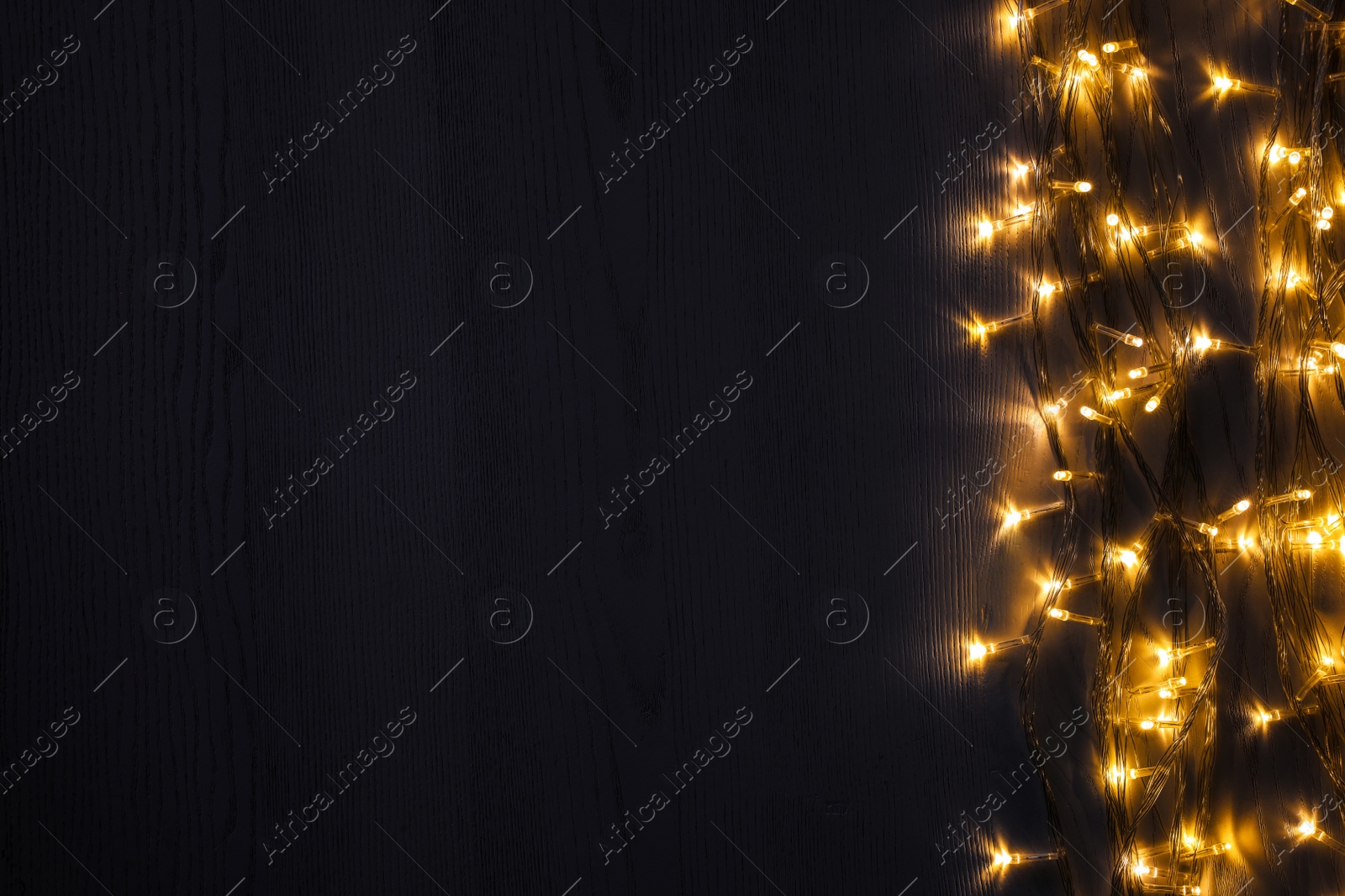 Photo of Beautiful glowing Christmas lights on wooden table, top view. Space for text