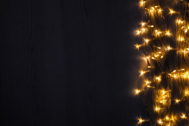 Photo of Beautiful glowing Christmas lights on wooden table, top view. Space for text