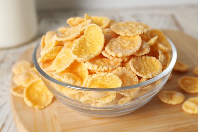 Photo of Glass bowl of tasty crispy corn flakes on wooden board, closeup