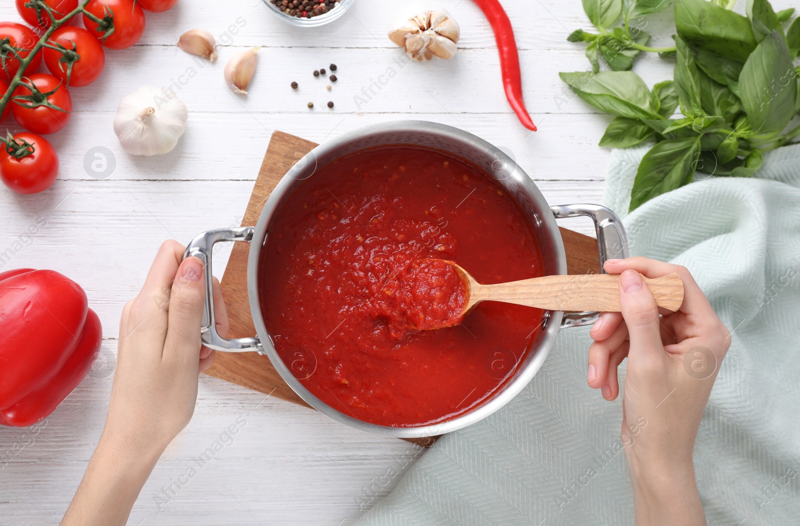 Photo of Woman cooking delicious tomato sauce at white wooden table, top view