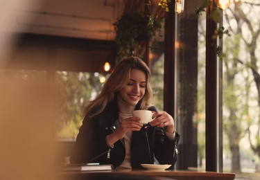 Photo of Young woman with cup of coffee at cafe in morning