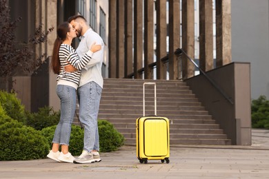 Photo of Long-distance relationship. Beautiful young couple kissing and suitcase near building outdoors