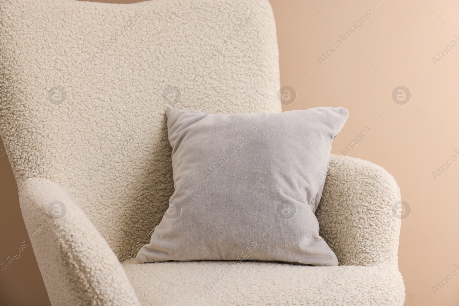 Photo of Soft grey pillow on armchair near beige wall