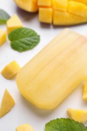 Photo of Tasty mango ice pop on white table, closeup. Fruit popsicle