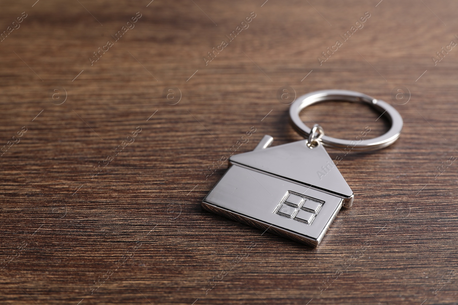 Photo of Metal keychain in shape of house on wooden table, closeup. Space for text